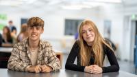 To elever fra 10. klasse sidder ved et bord og smiler til kameraet