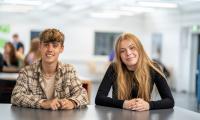 To elever fra 10. klasse sidder ved et bord og smiler til kameraet
