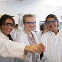 Tre piger i kitler i kemilokalet