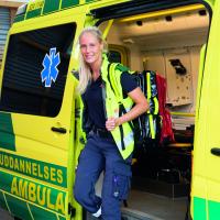 Kvindelig ambulancebehandler med udstyr står ved ambulance